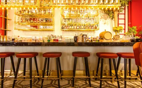 Bar con botellas doradas y taburetes rojos. Ideas para decorar un bar con poco dinero: ¡la iluminación y los detalles marcan la diferencia!
