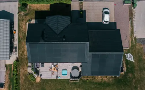 Villa med solceller och ett modernt batterilager. Uteplats med spabad och utemöbler. En vit bil parkerad på uppfarten.