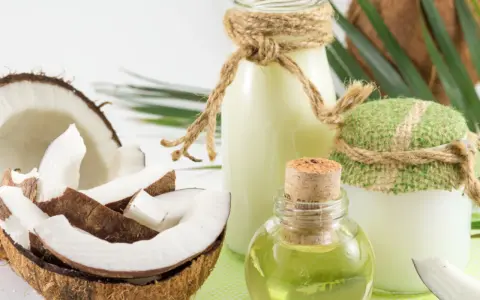 Aceite de coco para el pelo en frascos y botellas, junto a cocos frescos y hojas verdes.