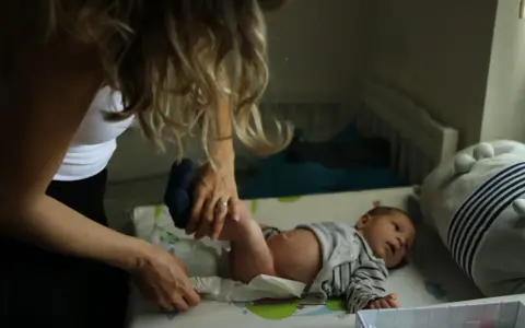 Mama zmienia pieluszkę noworodkowi. Zastanawiasz się, ile kupić pieluszek dla noworodka? Warto mieć zapas!