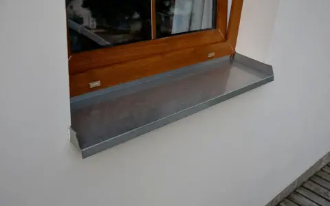Szary parapet zewnętrzny plastikowy pod drewnianym oknem.