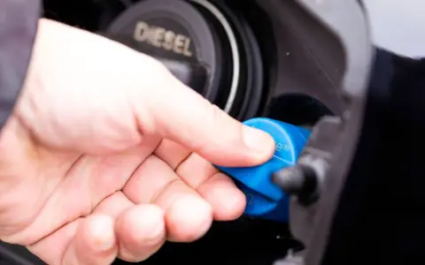 Hand schraubt blauen AdBlue-Deckel auf Diesel-Tanköffnung. AdBlue ist eine Harnstofflösung zur Abgasreinigung bei Dieselfahrzeugen.