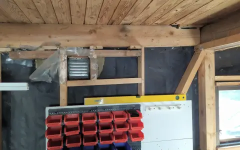 Pågår arbete för att isolera garage. Syns träbjälkar, isolering och förvaringssystem med fack.