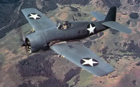 F6F Hellcat fliegt über hügelige Landschaft.