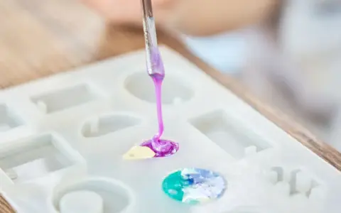 A person is learning how to make an epoxy resin mold by carefully pouring colored resin into a silicone mold.