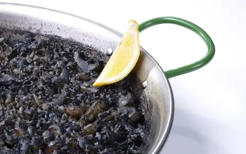 Arroz negro en paellera, con trozos de calamar y un gajo de limón.