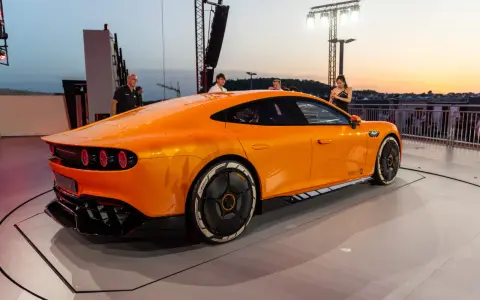 Ein leuchtend oranger AMG GT XX steht auf einer Bühne, beleuchtet vom Abendhimmel.
