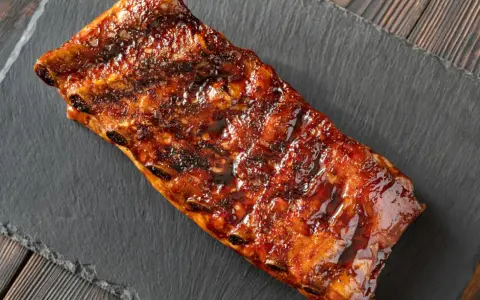 Costillas a la miel, glaseadas y jugosas, servidas sobre una pizarra oscura.