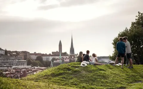 Vänner njuter av utsikten över Haga, Göteborg. En grupp unga människor sitter på en gräskulle med staden i bakgrunden.