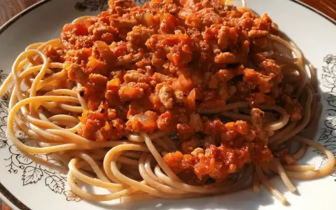 Porcja pysznego spaghetti bolognese z aromatycznym sosem mięsnym i pomidorowym, podana na talerzu z ozdobnym wzorem.