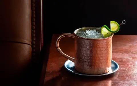 Chłodny Moscow Mule lub London Mule w miedzianym kubku, ozdobiony plasterkiem limonki, na drewnianym blacie.