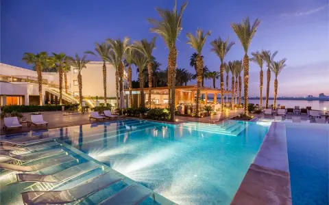 Luxury resort pool with palm trees and lounge chairs at dusk.