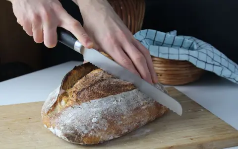Krojenie świeżego chleba na desce. Idealna temperatura, w jakiej piec chleb, to klucz do jego chrupkości.
