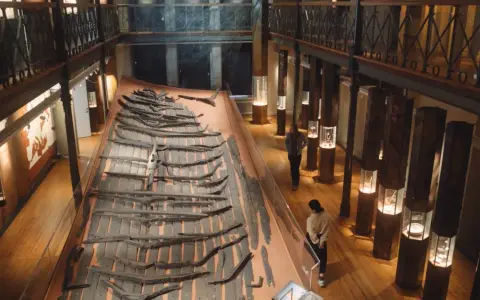 Vikingaskeppsvrak på ett museum i Göteborg. Besökare studerar utställningen med gamla trädelar.