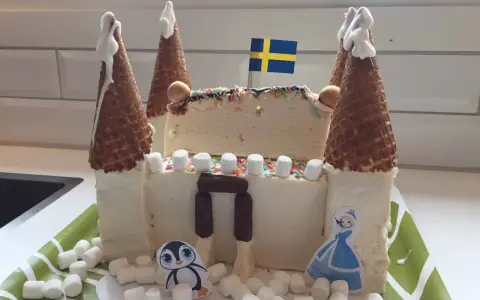 En fantasifull glasstårta slott med svenska flaggan, marshmallows och en söt pingvin.