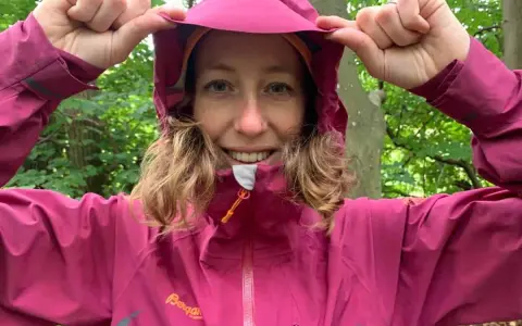 Kvinna i skogen drar upp huvan på sin rosa jacka, redo för 5000 vattenpelare.