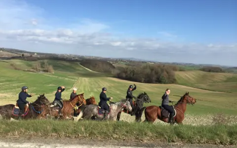 Un gruppo di persone in sella a cavalli attraversa un paesaggio collinare verdeggiante, godendosi le loro vacanze a cavallo sotto un cielo azzurro.