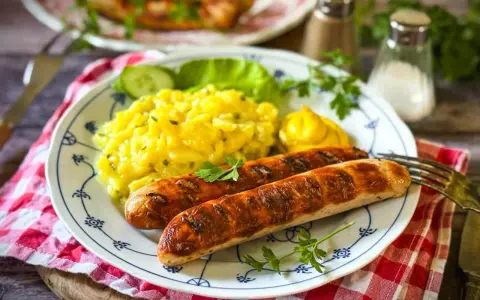 Zwei gegrillte Bratwürste mit Kartoffelsalat und Senf. Ein leckeres Rezept für Bratwurst selber machen.