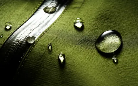 Gocce d'acqua su tessuto verde, dimostrando il significato di "water repellent".