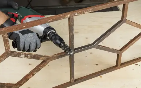 Rękawica z metalową szczotką na wiertarce usuwa rdzę z metalowej konstrukcji. Skuteczny sposób, jak odrdzewić metal.