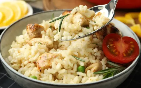 Kremowe risotto z kurczakiem, groszkiem i rozmarynem, udekorowane pomidorkiem. Idealne na obiad.