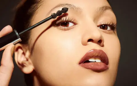 Una mano aplica máscara de pestañas a unos ojos pequeños, resaltando su belleza natural.