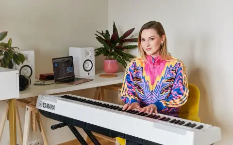Kobieta gra na pianinie Yamaha. W tle laptop i głośniki, idealne do nauki śpiewu dla dzieci.