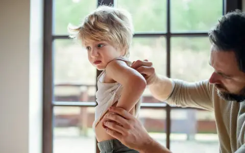 Un père examine le dos de son enfant, peut-être pour vérifier une poussée d'eczéma.