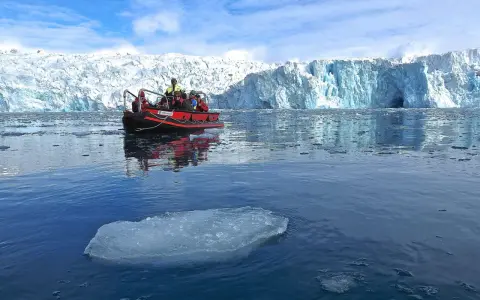 Ein Schlauchboot mit Touristen fährt auf dem eisigen Meer vor einem riesigen Gletscher. Ein wahrer "ice express" in die Arktis.