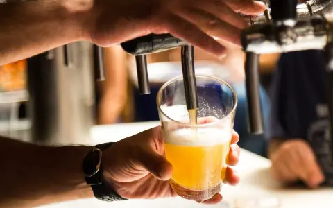 Ręka nalewa złociste piwo do szklanki. Czy alkoholik może pić piwo bezalkoholowe? To pytanie, na które odpowiedź zależy od indywidualnej sytuacji.