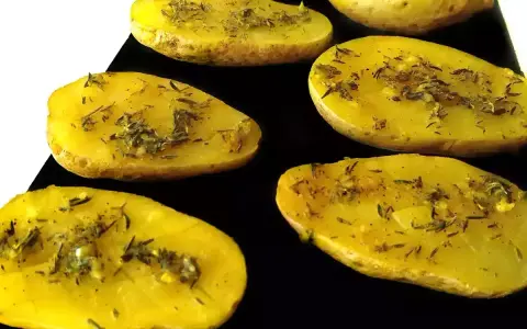 Patatas al microondas cortadas por la mitad, sazonadas con hierbas y especias, listas para cocinar.