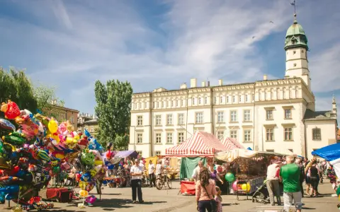Kolorowy jarmark na rynku na Kazimierzu w Krakowie. Balony, stragany z pamiątkami i ludzie spacerujący pod jasnym niebem.
