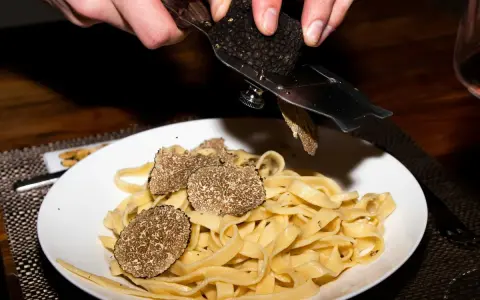 Dłonie trą całe grzyby trufle nad talerzem tagliatelle.