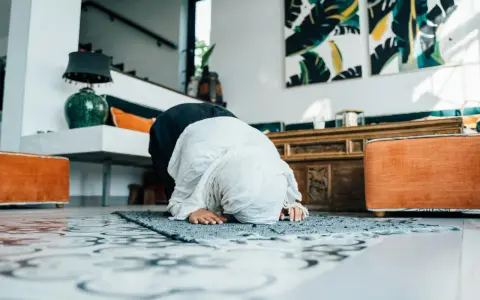 Kobieta w hidżabie klęczy na dywaniku, wykonując modlitwy o pokój. W tle widać nowoczesne wnętrze z dziełami sztuki.