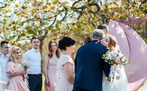 Wzruszające życzenia dla młodej pary. Panna młoda tuli się do ojca, a goście patrzą z uśmiechem.
