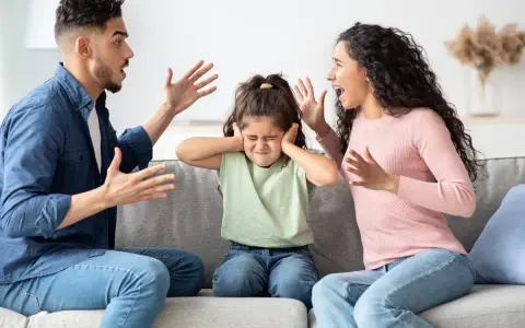 Ein Kind hält sich die Ohren zu, während die Eltern streiten. Eine Szene, die zeigt, wie schwierig es ist, wenn Eltern sich trennen.