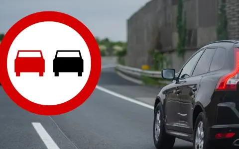 Znak zakazu wyprzedzania na drodze. Czarny SUV jedzie po prawej stronie, a z lewej widać znak z dwoma samochodami.