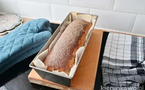Świeżo upieczony chleb cebulowy na zakwasie w keksówce, gotowy do wyjęcia. Obok rękawica kuchenna i ściereczka.