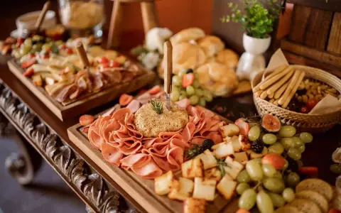 Stół z przekąskami: wędliny, sery, owoce, pieczywo i paluszki.