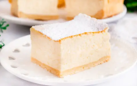 Puszysty sernik z mascarpone, oprószony cukrem pudrem, na białym talerzyku. Idealny na deser.