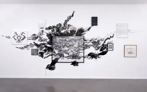 Œuvres d'Abdelkader Benchamma : une explosion d'encre noire sur mur blanc, encadrée par des dessins et peintures.