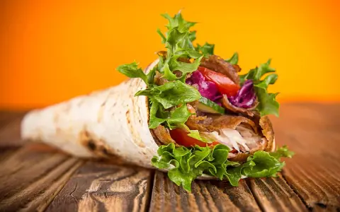 Un délicieux kebab maison garni de viande, salade croquante, tomates et chou rouge, sur un fond orange vif.
