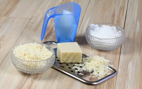 Ingrédients pour une lessive maison : savon râpé, cristaux de soude et un bloc de savon sur une râpe.
