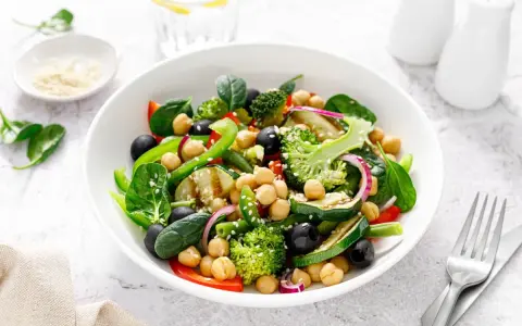 Ensalada de legumbres vibrante con garbanzos, brócoli, espinacas, aceitunas negras y pimientos verdes.
