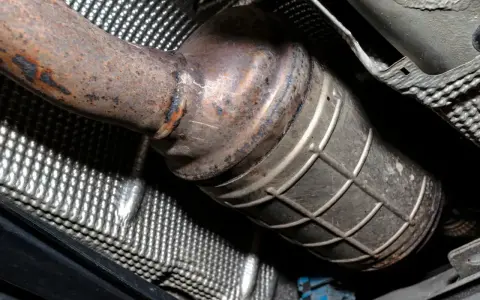 Widok z dołu na skorodowany, stopiony katalizator samochodowy z widocznymi śladami rdzy i uszkodzeń.
