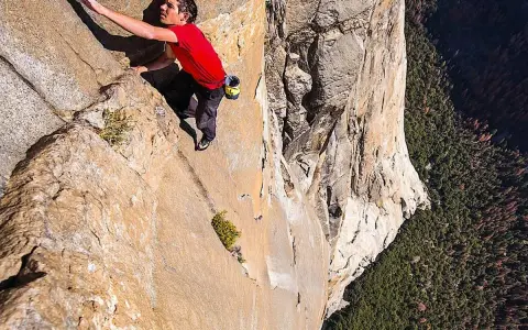 Ein Mann klettert free solo eine steile Felswand empor, mit einem tiefen Abgrund unter ihm.