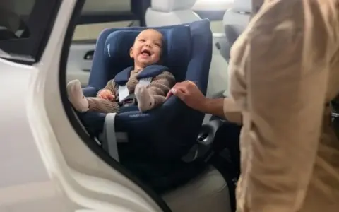 Bebé sonriente en un maxicosi azul, listo para aprender como colocar el maxicosi en el coche.