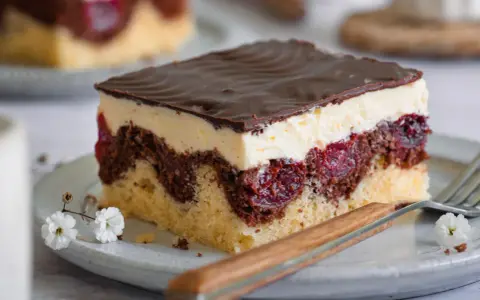 Ein Stück Donauwelle-Kuchen mit Schokoladenglasur, Sahne und Kirschen. Dieses Rezept ist ein Klassiker.
