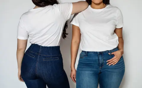 Dwie kobiety w białych T-shirtach i jeansach. Jedna ma na sobie ciemne jeansy z wysokim stanem, podkreślające szerokie biodra stylizacje.