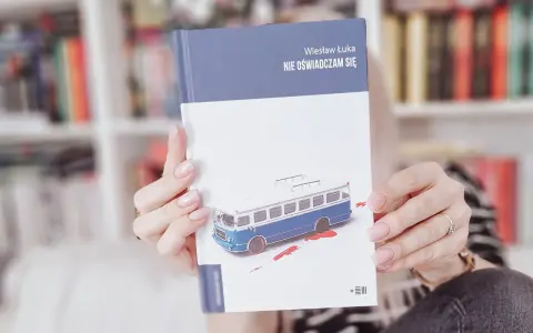 Dłonie trzymają książkę "Nie oświadczam się" z okładką przedstawiającą niebieski autobus i plamy krwi.